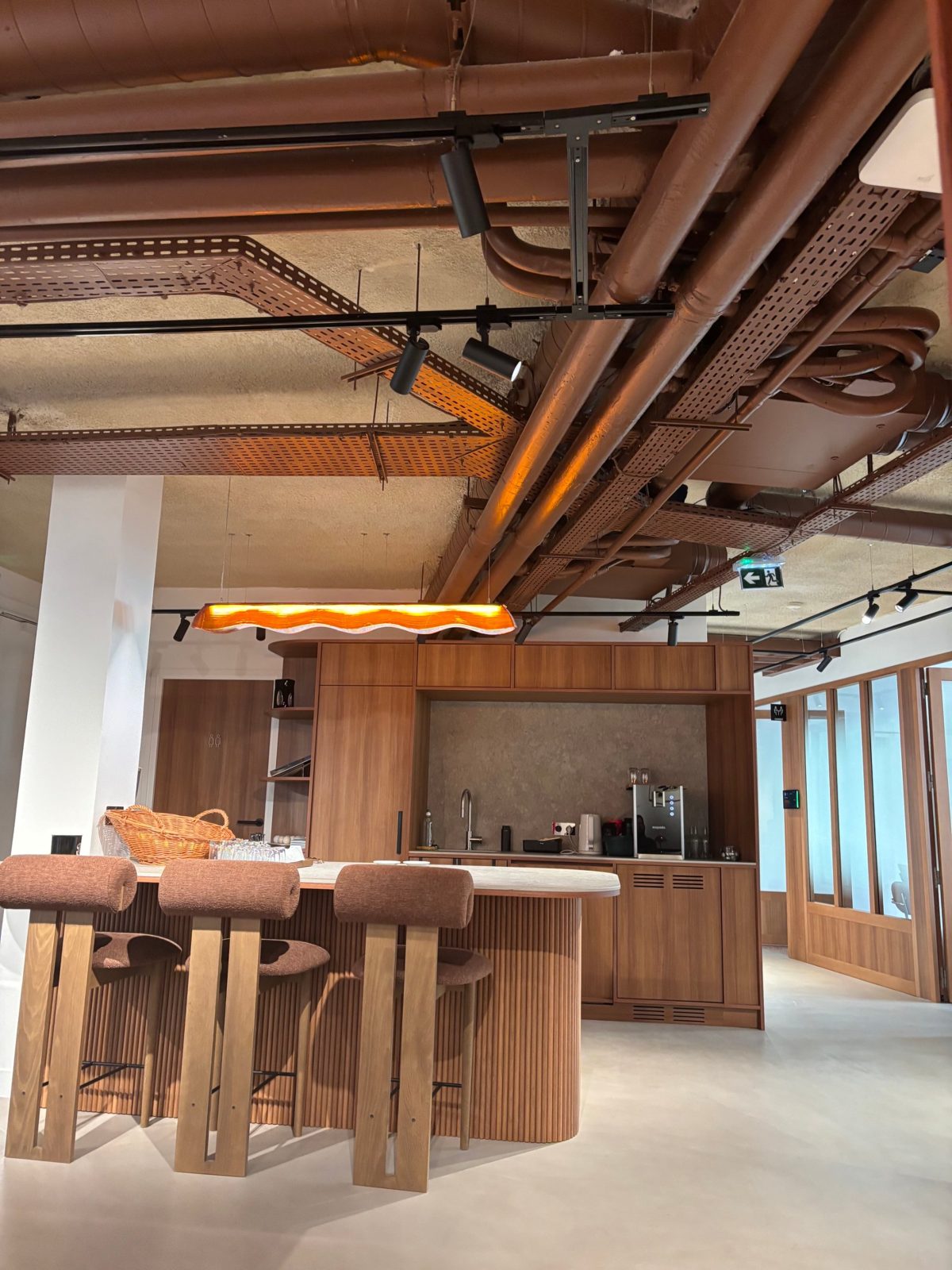 Coin café de bureaux d’entreprise à Paris : îlot cannelé en bois, tabourets en bouclette terracotta et suspension ambrée