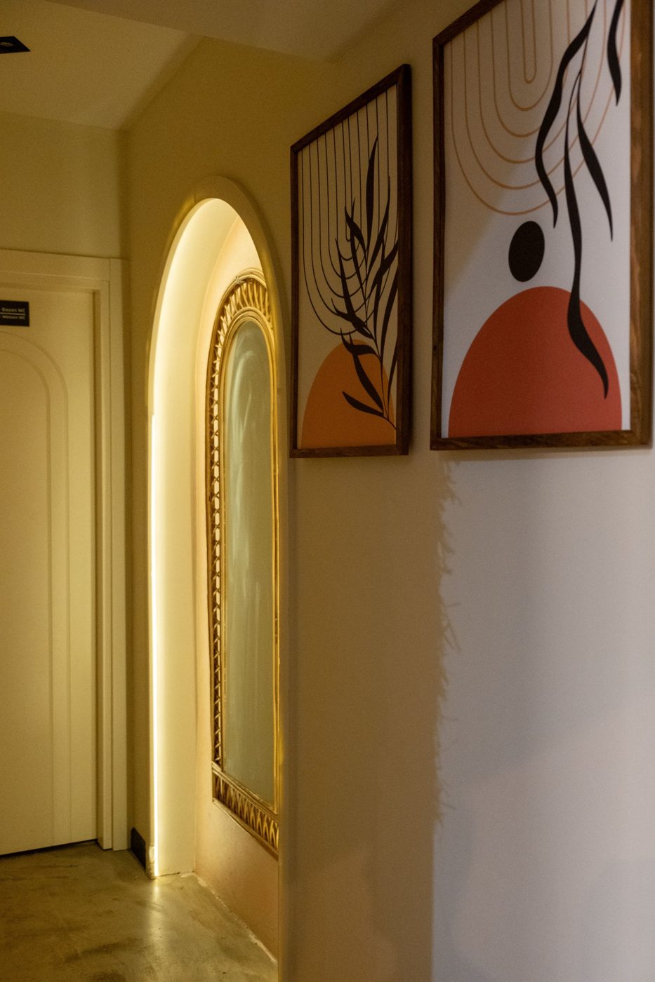 Couloir avec niche en arche rétroéclairée, miroir à cadre en rotin et affiches graphiques aux tons terracotta