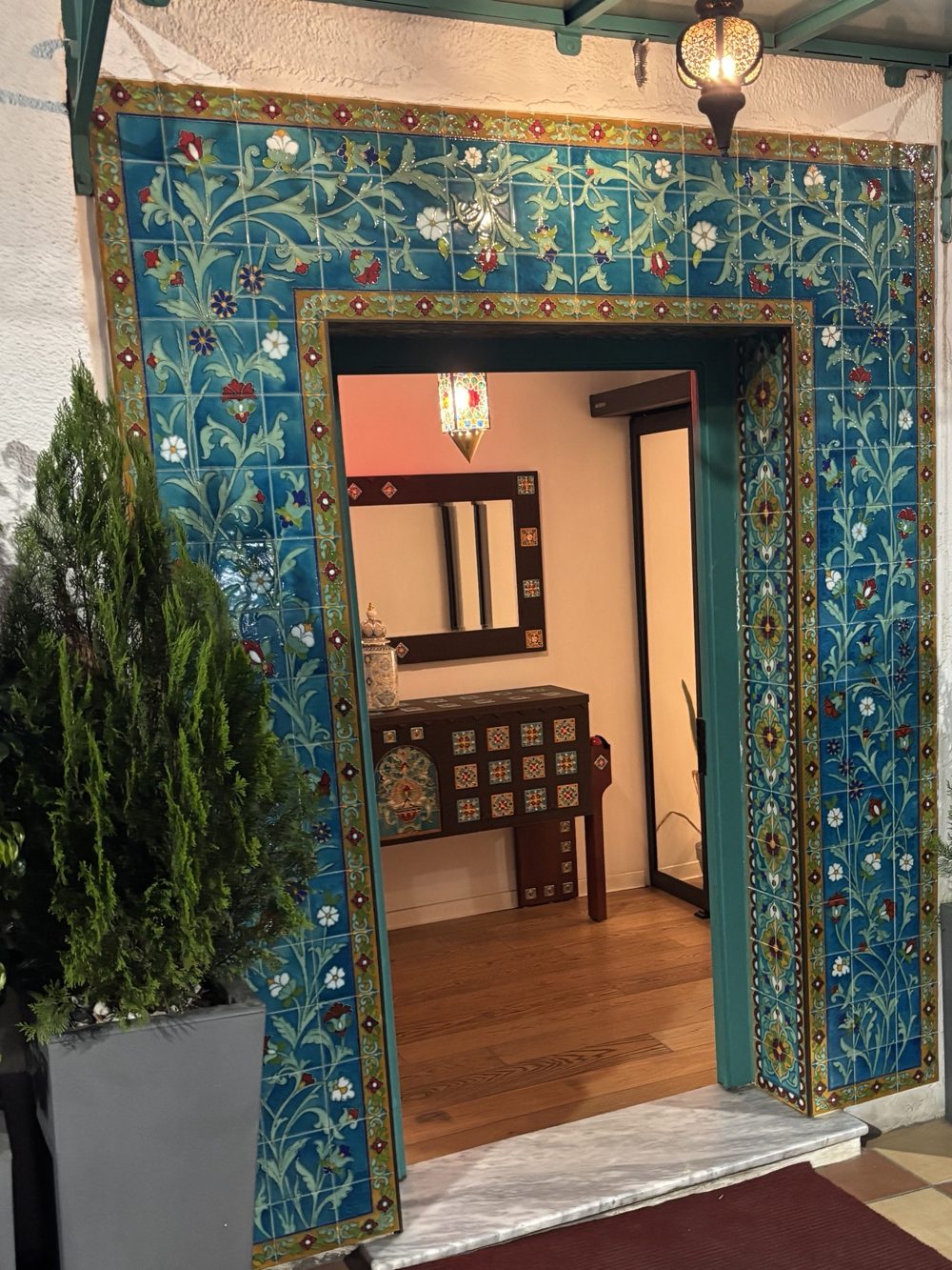 Entrée encadrée de carreaux de céramique turquoise à motifs floraux, console marquetée et lanterne ciselée